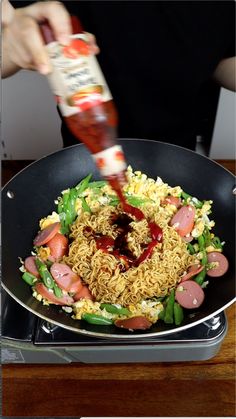 someone pouring ketchup on some food in a frying pan