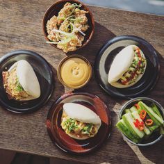 four plates with food on them sitting on a wooden table next to some dipping sauces