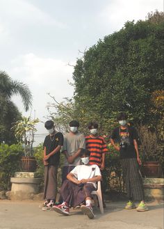 a group of young men standing around each other in front of some trees and bushes