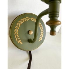 a green wall light with a white and gold design on the front, attached to a black cord