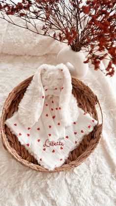 a basket filled with white towels and red hearts on top of a bed next to a vase