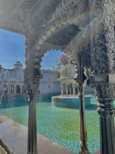 an ornate fountain in the middle of a courtyard with arches and pillars, surrounded by blue water