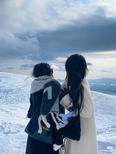 two women standing on top of a snow covered slope with their backs to each other