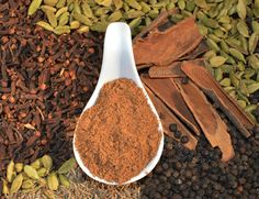 a spoon full of cinnamon powder next to some spices and herbs on the ground,