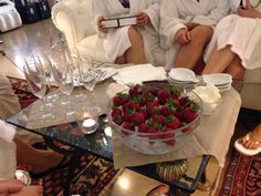 two women in white robes sitting on a couch with strawberries and wine glasses around them