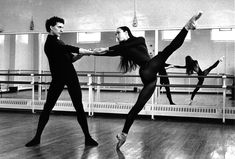 two dancers in black leotards and one is holding his leg up while the other dancer