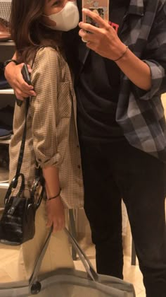 a man and woman standing next to each other in front of a luggage bag while looking at their cell phones