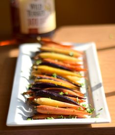 carrots and other vegetables are on a white plate next to a bottle of maple syrup