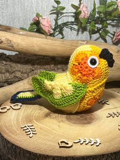 a yellow and green bird sitting on top of a piece of wood with flowers in the background