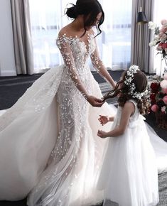 two women in wedding gowns standing next to each other and one is holding the bride's hand