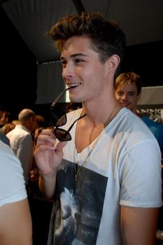 a young man is smiling while holding onto his glasses in front of other people at an event