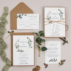 the wedding stationery is laid out with greenery