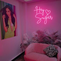 a pink couch in front of a neon sign that says hey sugar