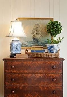 an old dresser with a lamp and painting on the wall