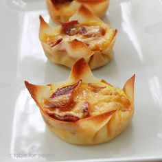 three small pastries on a white plate with plastic wrappers around them and bacon in the middle