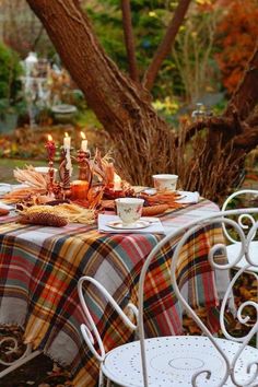 an outdoor table set for two with fall leaves and teacups in the foreground