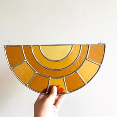 a hand is holding up a stained glass suncath in front of a white wall