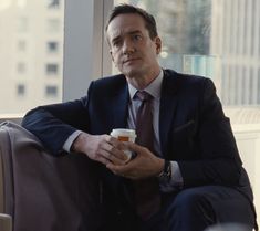 a man in a suit and tie sitting on a couch with a cup of coffee