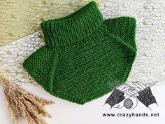 a green knitted sweater sitting on top of a table next to some dried flowers