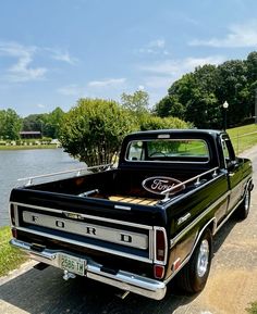 an old black truck parked on the side of a road next to a body of water