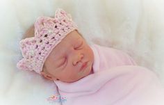 a newborn baby wearing a pink crochet hat and sleeping on a white blanket