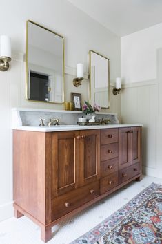 a bathroom vanity with two mirrors above it and a rug on the floor next to it