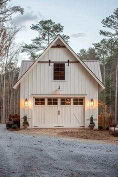 a white house with two garages and lights on the front door is surrounded by pine trees