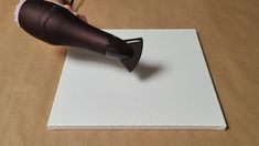 a person using a hair dryer on top of a piece of paper with a cord attached to it