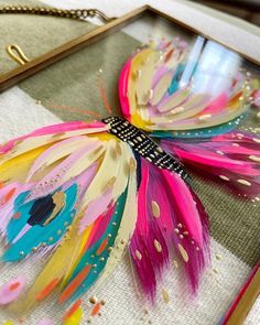 a colorful butterfly made out of feathers sitting on top of a piece of cloth next to a mirror