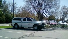 a white police truck parked in a parking lot next to a tree and some cars