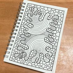 a spiral notebook with an intricate design on the front and back cover, sitting on a wooden surface