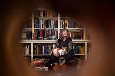 a woman sitting in front of a bookshelf holding a cat