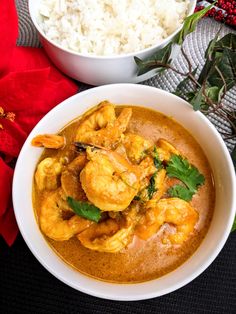 a bowl filled with chicken and spinach curry next to rice on a wooden table