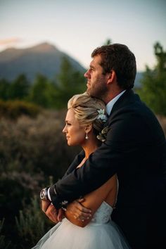 a bride and groom embracing each other in the mountains