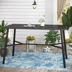 an outdoor table with potted plants on the floor and a blue rug in front of it