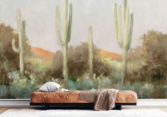 a painting of cactus trees in front of a wall with a bed and throw blanket