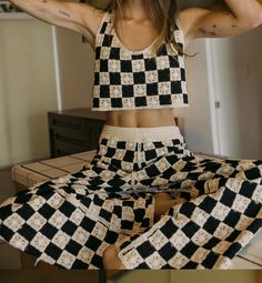 a woman sitting on top of a bed wearing black and white checkered pants with her hands behind her head