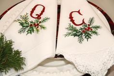 two white christmas napkins on top of a plate with holly and red berries embroidered on them