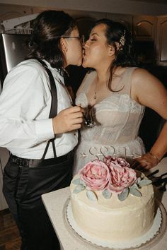 two people kissing each other while standing in front of a cake with flowers on it