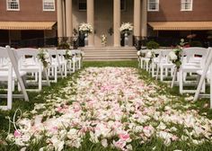 the aisle is lined with white chairs and pink flowers in front of a large building