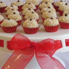 a white cake with red ribbon and cupcakes on it