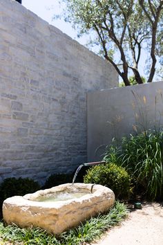 a stone fountain in front of a brick wall and shrubbery with water running from the faucet