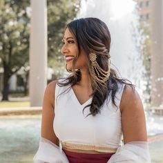 a woman in a white top and red skirt standing next to a fountain with water spouting from it