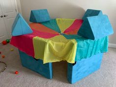 a child's play table made out of cardboard blocks and colored cloths, in a room with toys on the floor