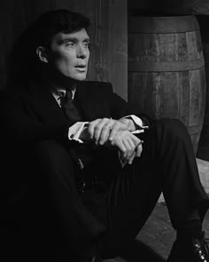 a man in a suit and tie sitting on the ground next to two wooden barrels