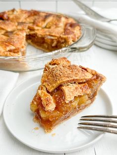 a slice of apple pie on a plate next to a fork and glass dish with one slice missing