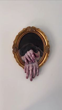 a person's hand reaching out from behind a gold framed mirror on the wall