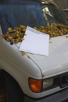 a white truck with leaves on the hood and paper stuck to it's windshield