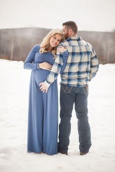 a pregnant couple standing in the snow together