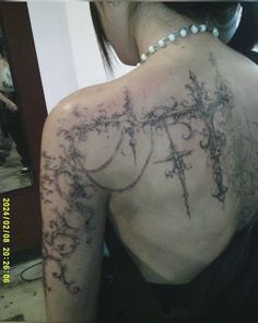 the back of a woman's tattoo with vines and pearls on her shoulder,